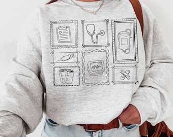 May include: A gray sweatshirt with a black outline of medical symbols in squares. The symbols include a stethoscope, a heart monitor, a syringe, bandages, a clipboard, and an IV bag.