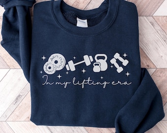 May include: A navy blue sweatshirt with a white graphic of weights and the text "In my lifting era".