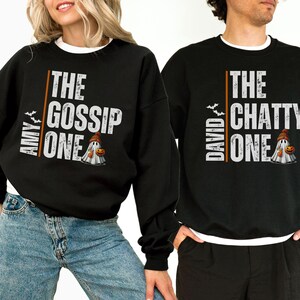 May include: Two black sweatshirts with a ghost graphic and text. The first sweatshirt says "Amy The Gossip One" and the second sweatshirt says "David The Chatty One".
