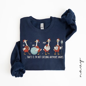 May include: Navy blue sweatshirt with a whimsical design of geese in Santa hats, each in a different pose, with the text "...THAT'S IT, I'M NOT CATCHING ANYMORE BABIES." A fun, festive garment.