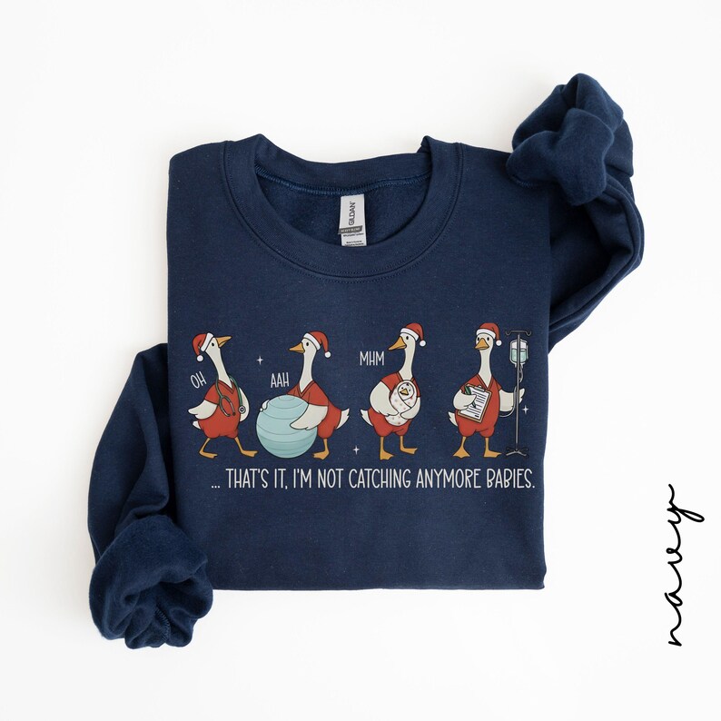 May include: Navy blue sweatshirt with a whimsical design of geese in Santa hats, each in a different pose, with the text "...THAT'S IT, I'M NOT CATCHING ANYMORE BABIES." A fun, festive garment.