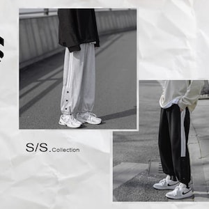 May include: Two people wearing sweatpants with side stripes. The person on the left is wearing white sweatpants with a button detail and white sneakers. The person on the right is wearing black sweatpants with white stripes and white sneakers. The text "S/S.Collection" is visible in the image.