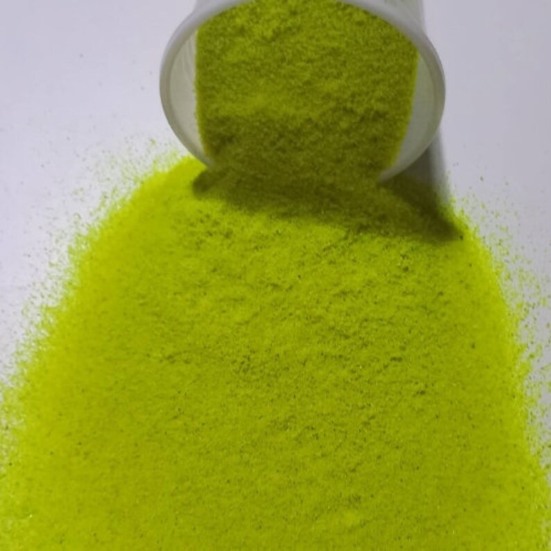 May include: A close-up of a bright green glitter, poured out of a container onto a white surface.