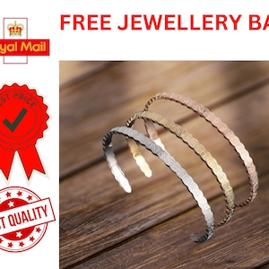 May include: Three gold-toned bracelets with a wavy, textured design. The bracelets are stacked on top of each other on a wooden surface.