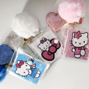以下が含まれることがあります： 異なるキャラクターデザインの透明なプラスチック製ノート5冊。各ノートには、ラインストーンがついたハート型のチャームと、金色のチェーンに付いたふわふわのポンポンが付いています。キャラクターは、ハローキティ、マイメロディ、クロミです。