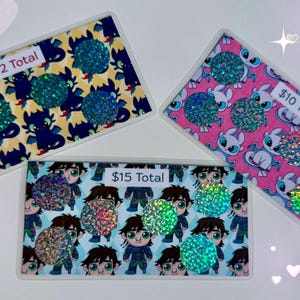 May include: Three rectangular, decorative items with cartoon character designs and glitter accents. One has a blue and yellow dragon pattern, another a pink and white dragon pattern, and the third features a cartoon boy. Each has a glittery embellishment.