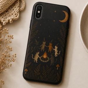 May include: A black smartphone case featuring a printed illustration of five cats wearing pointed hats dancing in a circle around a campfire. The design includes a golden crescent moon, small stars, ferns, and mushrooms against a dark background.