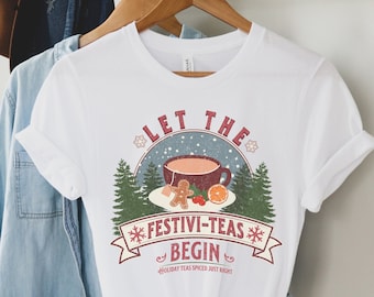 May include: White t-shirt with a vintage-style graphic design featuring a mug of hot beverage, a gingerbread man, and an orange slice. The text reads "Let the Festivi-Teas Begin" with the tagline "Holiday Teas Spiced Just Right".