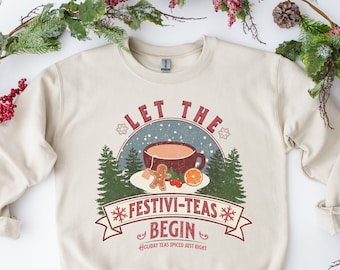 May include: A beige sweatshirt with a vintage-style graphic design featuring a mug of hot beverage, a gingerbread man, and the text "Let the Festivi-Teas Begin". The text "Holiday Teas Spiced Just Right" is also included in the design.
