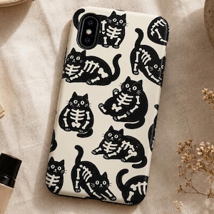 Puede incluir: Una funda rectangular para smartphone con fondo color crema que presenta un patrón repetitivo de gatos negros con ilustraciones blancas de cajas torácicas y huesos. La funda tiene un recorte negro para la cámara y bordes redondeados.