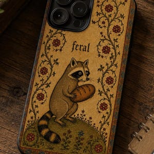 K&ouml;nnte beinhalten: Eine rechteckige Handyh&uuml;lle mit beigem Hintergrund und einer zentralen Illustration eines Waschb&auml;ren, der ein Brot h&auml;lt. Das Wort feral ist &uuml;ber dem Waschb&auml;ren aufgedruckt. Das Design umfasst florale Ranken und einen dekorativen Rand.