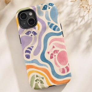 Puede incluir: Una funda para smartphone con un patr&oacute;n de acuarela repetitivo de mapaches integrados en l&iacute;neas onduladas y fluidas de colores pastel, incluyendo morado, azul, rosa, naranja y verde sobre un fondo crema con un recorte negro para la c&aacute;mara.