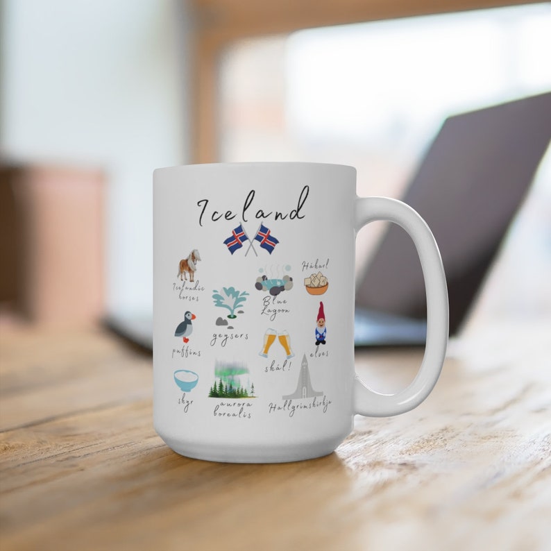 K&ouml;nnte beinhalten: Ein wei&szlig;er Keramikbecher mit dem Schriftzug Iceland und Illustrationen isl&auml;ndischer Kultursymbole, darunter Pferde, Papageientaucher, Geysire, die Blaue Lagune, Skyr, Nordlichter, Biergl&auml;ser, ein Gnom und die Hallgr&iacute;mskirkja mit zwei Flaggen.