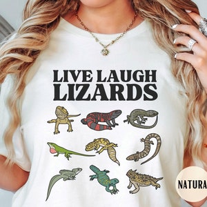 May include: White t-shirt with the text "LIVE LAUGH LIZARDS" in black. The shirt features a variety of colorful lizards, including a bearded dragon, a red-headed lizard, a gecko, and a horned lizard.