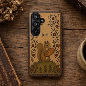 May include: A rectangular phone case with a tan background featuring a central illustration of a squirrel holding a loaf of bread. The word feral is printed above the squirrel in black text, surrounded by decorative floral vines and a border.