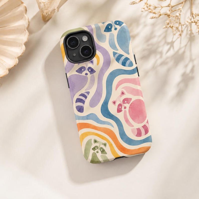 Puede incluir: Una funda para smartphone con un patr&oacute;n de acuarela repetitivo de mapaches integrados en l&iacute;neas onduladas y fluidas de colores pastel, incluyendo morado, azul, rosa, naranja y verde sobre un fondo crema con un recorte negro para la c&aacute;mara.
