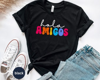 May include: Black t-shirt with the text "hola amigos" in rainbow colors. The text is in a retro, wavy font.