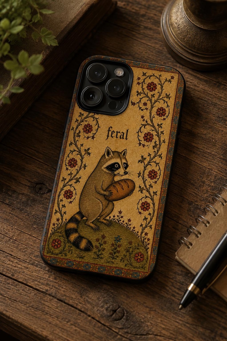 K&ouml;nnte beinhalten: Eine rechteckige Handyh&uuml;lle mit beigem Hintergrund und einer zentralen Illustration eines Waschb&auml;ren, der ein Brot h&auml;lt. Das Wort feral ist &uuml;ber dem Waschb&auml;ren aufgedruckt. Das Design umfasst florale Ranken und einen dekorativen Rand.