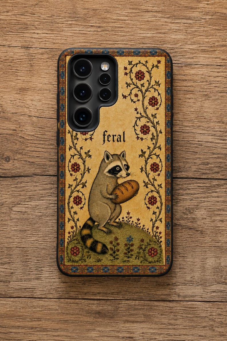 K&ouml;nnte beinhalten: Eine rechteckige Handyh&uuml;lle mit beigem Hintergrund und einer zentralen Illustration eines Waschb&auml;ren, der einen Laib Brot h&auml;lt. Das Wort feral ist &uuml;ber dem Waschb&auml;ren aufgedruckt. Das Design umfasst florale Ranken und eine blau-orange Schmuckbord&uuml;re.