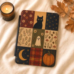 May include: A rectangular e-reader case featuring a patchwork design of nine squares. Patterns include a black cat, a white ghost, a pumpkin, a crescent moon, stars, flowers, mushrooms, acorns, and plaid. The case has a black spine and stylus holder.