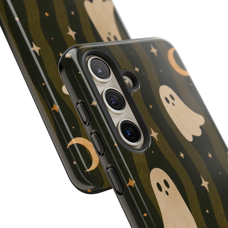 May include: A dark olive green phone case featuring a repeating pattern of beige ghosts, golden crescent moons, and small four-pointed stars. The case has a glossy finish and includes precise cutouts for a triple-lens camera system and side buttons.