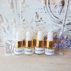 May include: Four small clear glass bottles with gold-colored caps and white dropper tops, each featuring a white label with black text reading Radiance, Refresh, Rejuvenate, and Reborn, all contained within a clear plastic bag for storage.