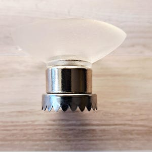 May include: A clear, frosted glass soap dish with a silver-colored metal base. The dish has a shallow, curved bowl shape. The base has a cylindrical section and a decorative, scalloped edge. The soap dish is designed to hold a bar of soap.
