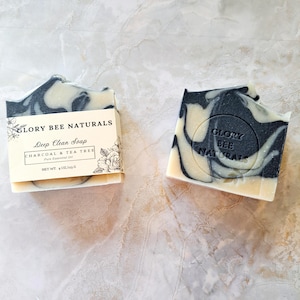 May include: Two bars of soap with a marbled black and white design. One bar is in its packaging, which features the text "Glory Bee Naturals Deep Clean Soap Charcoal & Tea Tree Pure Essential Oil". The soap weighs 4 oz.