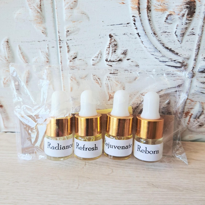 May include: Four small glass dropper bottles with gold-colored collars and white rubber bulbs, encased in a clear plastic bag. Each bottle features a white label with black text reading Radiance, Refresh, Rejuvenate, and Reborn respectively.