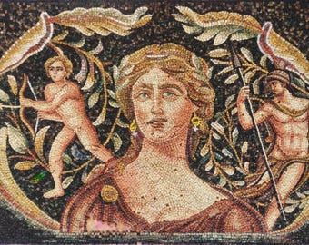 Op de afbeelding: Een mozaïekkunstwerk dat een centrale vrouwelijke figuur met een lauwerkrans afbeeldt, geflankeerd door figuren met een boog en een speer. Het mozaïek heeft een donkere achtergrond met bloemen- en bladeraccenten en is gemaakt van kleine, gekleurde tegels.