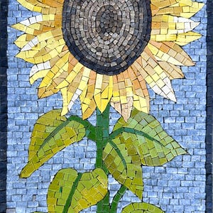 Può includere: Un'opera d'arte a mosaico raffigurante un girasole. Il fiore ha petali gialli, un centro marrone scuro e foglie verdi. Lo sfondo è un motivo blu chiaro, simile a mattoni, con un bordo scuro.