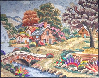 Puede incluir: Una obra de arte en mosaico que representa un paisaje sereno con un puente de piedra sobre un arroyo. La escena incluye varias casas con paredes de ladrillo rojo y tejados grises, rodeadas de árboles exuberantes y flores coloridas. Una cascada cae por una montaña en el fondo.