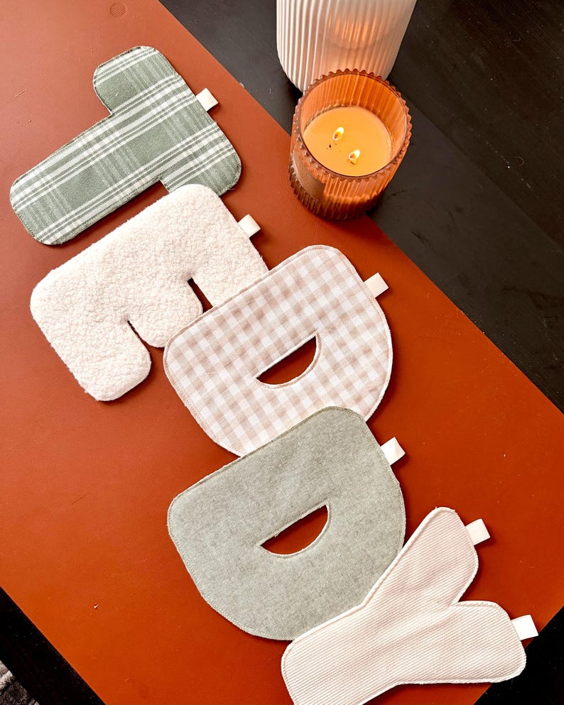 May include: A set of five fabric letters spelling the word "TODAY" in various textures and patterns. The letters feature sage green plaid, white sherpa, beige gingham, solid sage green, and cream corduroy, each with a small white fabric tag.