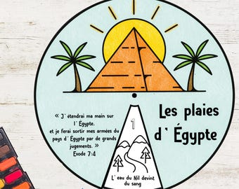 May include: A circular illustration with a pyramid, sun, and palm trees. Text in French reads "Les plaies d'Égypte" and a Bible verse. The illustration is on a light blue background with a white border. Watercolor paints and pencils are in the lower left corner.