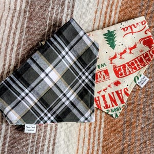May include: Two dog bandanas. One is a black, white, and gray plaid pattern. The other is cream-colored with a red and green Christmas design that says "Santa Believe". Both have a small white tag that says "Bear Creek Creations".
