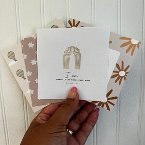 May include: A collection of square cards with various designs and text. The central card is white with a gold arched design and the words "I am fearfully and wonderfully made" printed below. Other cards feature floral and hot air balloon patterns.