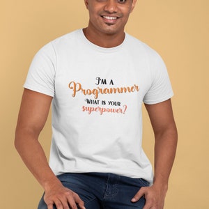 以下が含まれることがあります： オレンジと黒で「I'm a Programmer. What is your superpower?」と書かれた白いTシャツです。