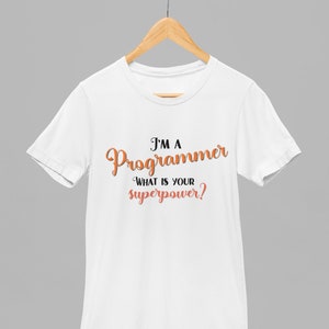 以下が含まれることがあります： 黒い文字とオレンジ色の文字で「I'm a Programmer What is your superpower?」と書かれた白いTシャツです。