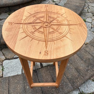May include: A round wooden table with a compass design carved into the top. The table has a simple, square base.
