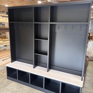 May include: Black entryway bench with a white top shelf and storage cubbies. The bench has a coat rack with hooks on each side.
