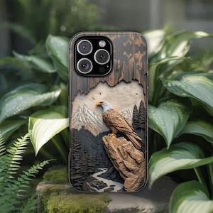May include: A smartphone case featuring a three-dimensional relief design of a bald eagle perched on a rocky cliff. The scene includes a mountain range, a forest of pine trees, and a winding river below, rendered in shades of brown, gray, and white.