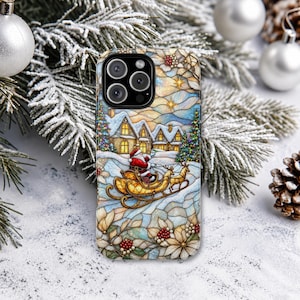 May include: A smartphone case featuring a stained glass style illustration of Santa Claus in a gold sleigh pulled by a reindeer. The scene includes a snow-covered village with lit windows, evergreen trees, and white poinsettia flowers with red berries.