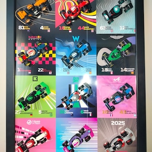 May include: A framed print showcasing miniature Formula 1 cars. Each car is set against a vibrant backdrop, with driver details and numbers. The black frame surrounds cars in red, blue, and green, among other colours.