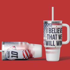 May include: Two white insulated tumblers with lids and straws. One upright, the other lying down. Both feature an American flag design and the text "I BELIEVE THAT WE WILL WIN." One tumbler displays the name "PULISIC" and the number "10."