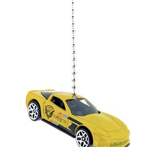 May include: Yellow toy car with black racing stripes and the text "HWCC Corvette Club" hanging from a silver chain.