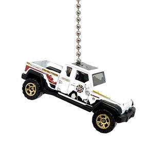 May include: White Jeep Gladiator pickup truck with black and gold accents, hanging from a silver chain. The truck has a "Jeep" logo and "Overland" text on the side.