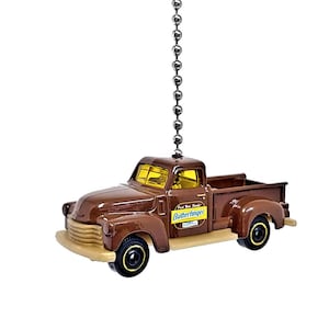 May include: A brown toy pickup truck with a yellow windshield and a "Butterfinger" logo on the side. The truck is hanging from a silver chain.