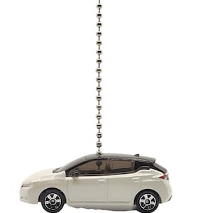 May include: A white and black toy car with a silver chain attached to the top. The car has black wheels and a black roof. The car is a miniature replica of a modern vehicle.