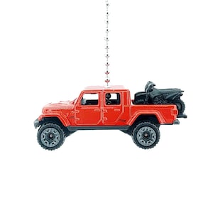 May include: A red toy truck with black wheels and a black ATV in the truck bed. The truck is suspended by a silver chain. The truck has the word "Rubicon" printed on the side.