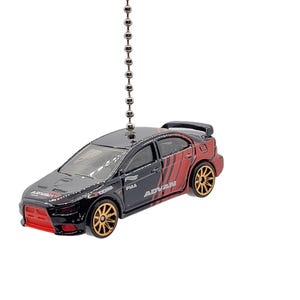 May include: A black and red toy car with gold wheels, hanging from a silver chain. The car has the word "ADVAN" printed on the side and a red front bumper. The car is a miniature replica of a sports car.